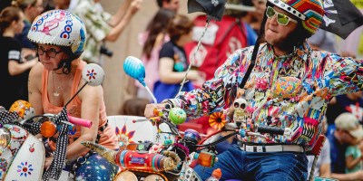 a picture of a couple riding scooters wearing eccentric costuming